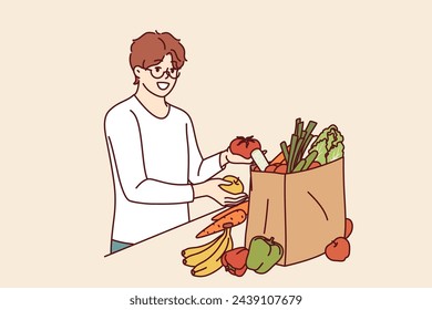 Vegetarian man takes out fresh vegetables and fruits from paper bag after going to farmer fair with eco-friendly goods. Peren vegan recommends eating high-quality vegetables without added pesticides