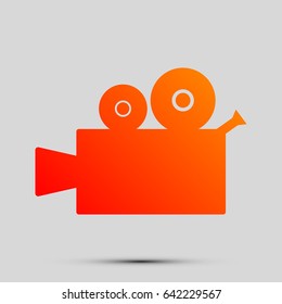 Video camera sign. Vector. Orange, red-yellow icon with shadow on gray background.