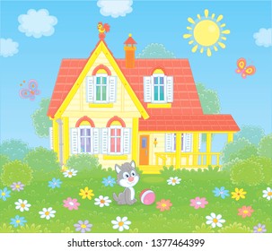 Village house and a small grey kitten playing with butterflies among flowers on green grass of a lawn, vector illustration in a cartoon style