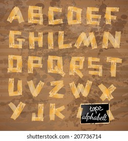 Vintage style alphabet made of yellow distressed tape with ink drops over a grunge beige background. 