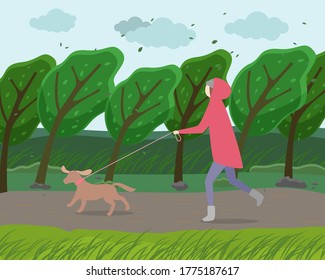 Walk with dog in the park. Woman is running with a doggy in garden strong windy weather. A happy pet walking with the owner against the backdrop of autumn landscape with a green trees bent to ground