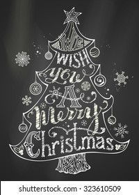 We Wish You a Merry Christmas. Chalk Merry Christmas Lettering in Christmas Tree Silhouette on blackboard background. Hand-written text, holly berry, Christmas balls, snowflakes, star on the top. 