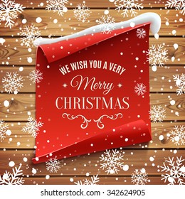 We wish you a very Merry Christmas, greeting card. Red, curved, paper banner on wooden planks with snow and snowflakes. Vector illustration.