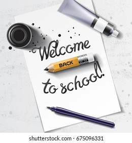 Welcome Back to School hand drawn lettering with calligraphy mockup with brush pen, sharp pencil, paint tube and black ink bottle on the background of white sheet of paper and grunge table