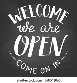 Welcome we are open. A welcome sign for cafes or shop visitors on blackboard background with chalk. Hand lettering