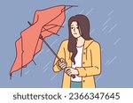 Wet woman stands with broken umbrella in heavy rain, and is sad because of cold and strong wind. Upset girl walking down street during storm and autumn rain needs waterproof clothes