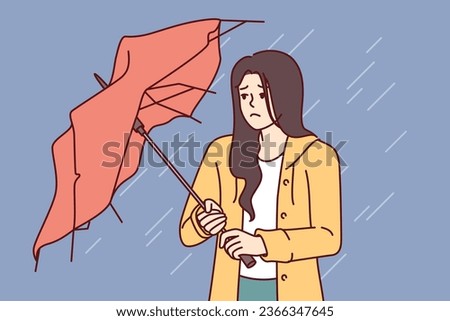 Wet woman stands with broken umbrella in heavy rain, and is sad because of cold and strong wind. Upset girl walking down street during storm and autumn rain needs waterproof clothes