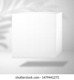 A white blank cubic box is above the surface. Shadow from a palm tree on the wall in the background. Mockup for design