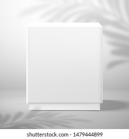 A white blank cubic box with a panel. Front view. Shadow from a palm tree on the wall in the background. Mockup for design