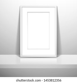 A white blank frame with passe-partout for a picture or poster stands near the wall on the shelf. Mockup for gallery design with shadow