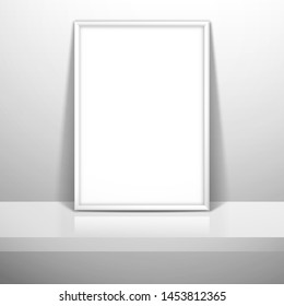 A white blank frame for a picture or poster stands near the wall on the shelf. Mockup for gallery design with shadow
