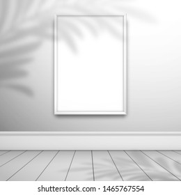 A white blank frame for a picture or poster on the wall in empty white room. The shadow of the palm tree is on top. Mockup for design