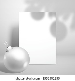 White blank greeting card, shadow from a fir-tree branch with toys and a white Christmas ball. Template for a festive New Year design