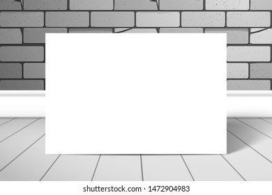 A white blank rectangle or sheet of paper stands near the brick wall on the plank floor. Mockup for design with shadow