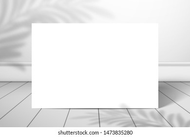 A white blank rectangle or sheet of paper stands near the wall on the plank floor. The shadow of the palm tree is on top. Mockup for design