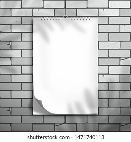 A white blank spiral notebook, album or calendar with a curved top sheet hangs on a brick wall. The shadow of the palm tree is on top. Mockup for design