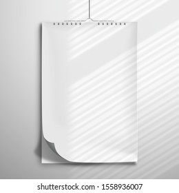 White blank spiral notebook, album or calendar hanging on the wall. The edge of the top sheet is bent. Mockup with realistic shadow from the blinds