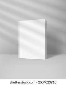 Libro blanco con portada dura en blanco con efecto de destello solar. Luz de la ventana con persianas