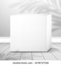 A white cubic box is near the wall on the plank floor. The shadow of the palm tree is on top. Realistic mockup for design