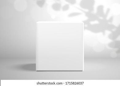 White cubic box on a background with a shadow from a branch of eucalyptus and bokeh