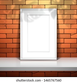 White empty frame with passepartout for a picture or a poster stands near the red brick wall on the shelf. The shadow of the monstera plant is on top. Mockup for design