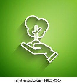 White line Tree in hand of environmental protection icon isolated on green background. Seed and seedling. Planting sapling. Ecology concept.  Vector Illustration
