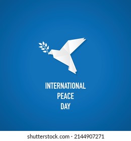 White origami dove silhouette and olive branch. International peace day background with paper bird isolated on blue background