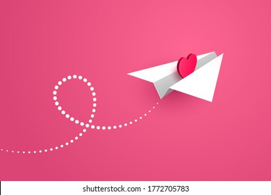 White paper airplane with red heart symbol inside is flying forward over pink background, white contrail is behind. Concept of love message, Valentine's day greetings, declaration of love