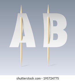 White paper cut font on toothpicks on grey background. A and B letters