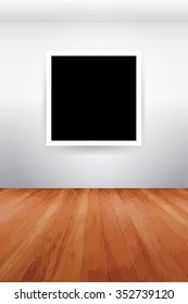 White picture frame with blank on white wall, wooden floor.