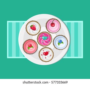  White plate with coloured cupcakes on green background . Top view.