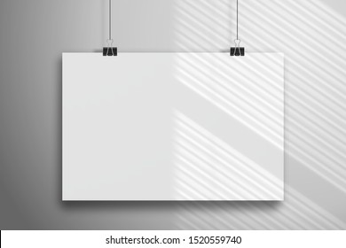 White sheet of paper hangs on the clamps. Mockup with shadow from the blinds