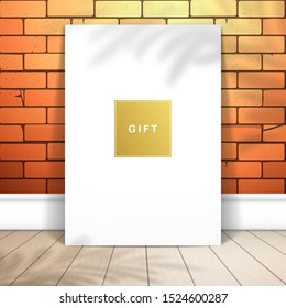 A white sheet of paper stands near a red brick wall on the boards. Gold label with the inscription Gift. Mockup for design with shadow of palm tree
