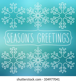 White snowflakes over blue square abstract smooth blur background with hand written season's greetings in a frame.