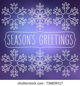 White snowflakes over blue square abstract smooth blur background with hand written season's greetings in a frame.