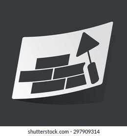 White sticker with black image of brick wall under construction, on black background