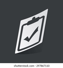 White sticker with black image of clipboard with tick mark, on black background