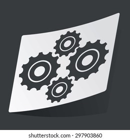 White sticker with black image of four cogs, on black background