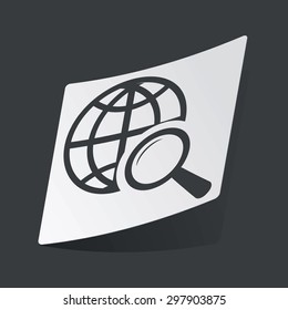 White sticker with black image of globe symbol under loupe, on black background