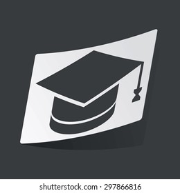 White sticker with black image of square academic hat, on black background