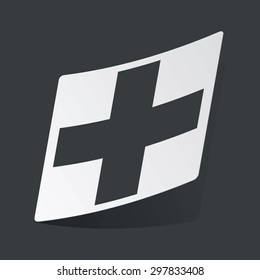 White sticker with black plus symbol, on black background