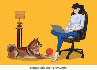 A white woman sits at home on a black armchair and works on a laptop. A dog sits at her feet.