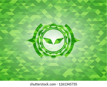 wings icon inside green emblem. Mosaic background