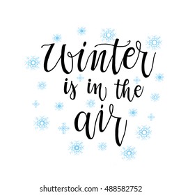 Winter is in the air  phrase for card. Hand drawn modern calligraphy. Ink illustration. Banner with hand drawn words. Isolated on white background with blue snowflake.