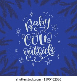 Winter mood lettering phrase Baby It’s Cold Outside on starry night sky framed with pine twigs. Festive handwritten with white message for print, apparel, poster, greeting card. Christmas quote.
