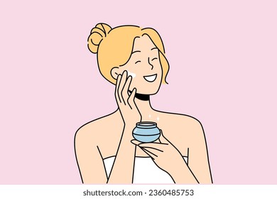 La mujer aplica crema antiedad para mantenerse hermosa, de pie en toalla de baño después de la ducha. Feliz rubia sonríe y usa crema cosmética para ayudar a prevenir arrugas y granos.