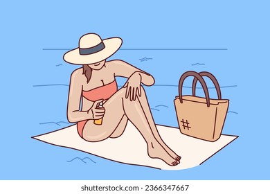 Woman applies sunscreen to protect herself from sun, relaxing on sea beach of tropical resort. Girl tourist uses sunscreen and counters ultraviolet rays, sitting on towel in hat and bikini