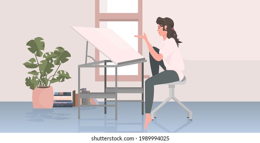 woman architect sitting at workplace with adjustable drawing board desk