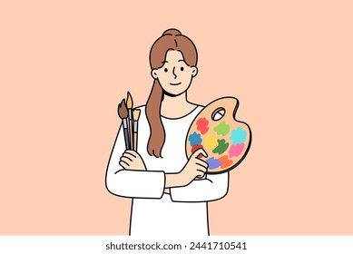 Woman artist holds brushes for painting and palette for mixing watercolor paints. Portrait of beautiful artist girl who is interested in creative hobby and wants to exhibit in art gallery