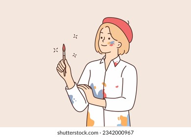 Woman artist in shirt stained with paint and beret holds brush and looks to side waiting for inspiration to create artwork. Girl artist doing creative work or making professional paintings